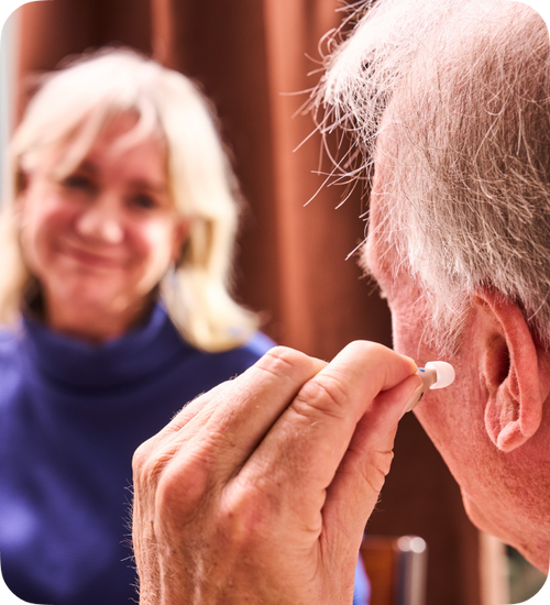 Man adjusting a hearing aid with a woman in the background