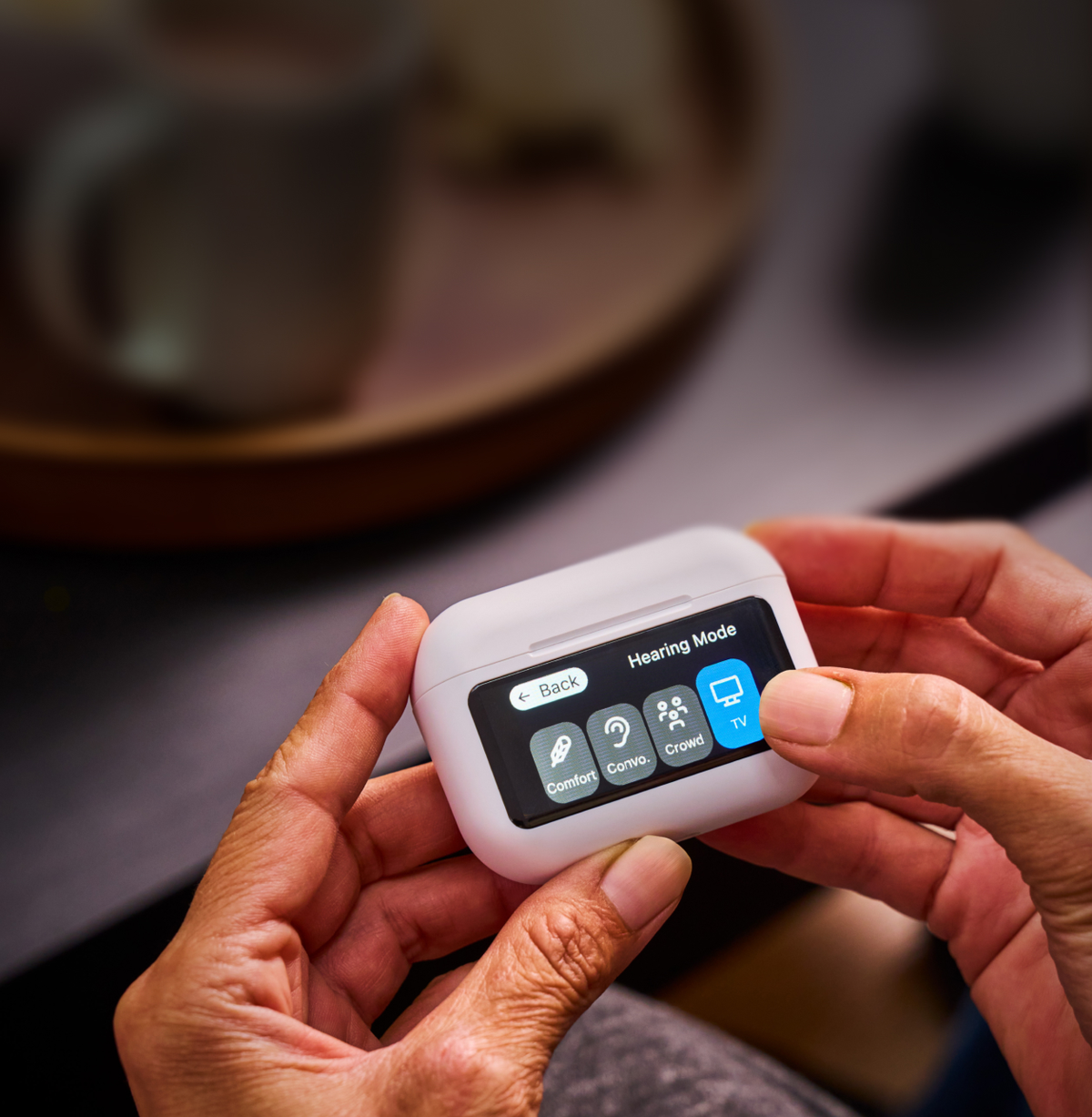 Person holding a white electronic device with a screen displaying options, on a blurred background of a table with a mug.